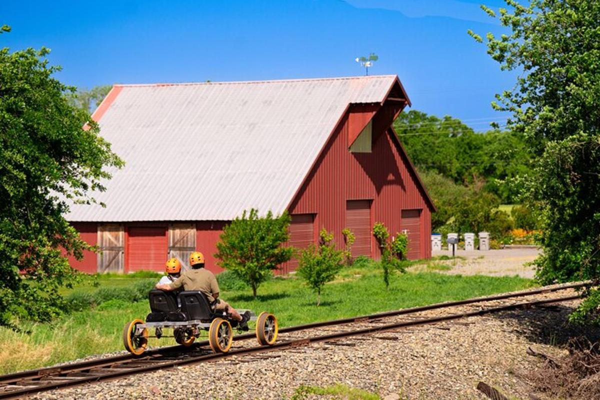 two people riding a toy train on the tracks next to a red barn