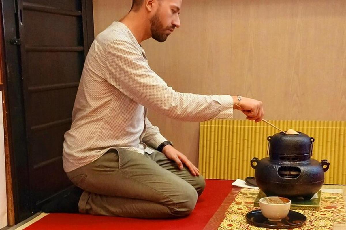 un uomo seduto sul pavimento che mescola una teiera