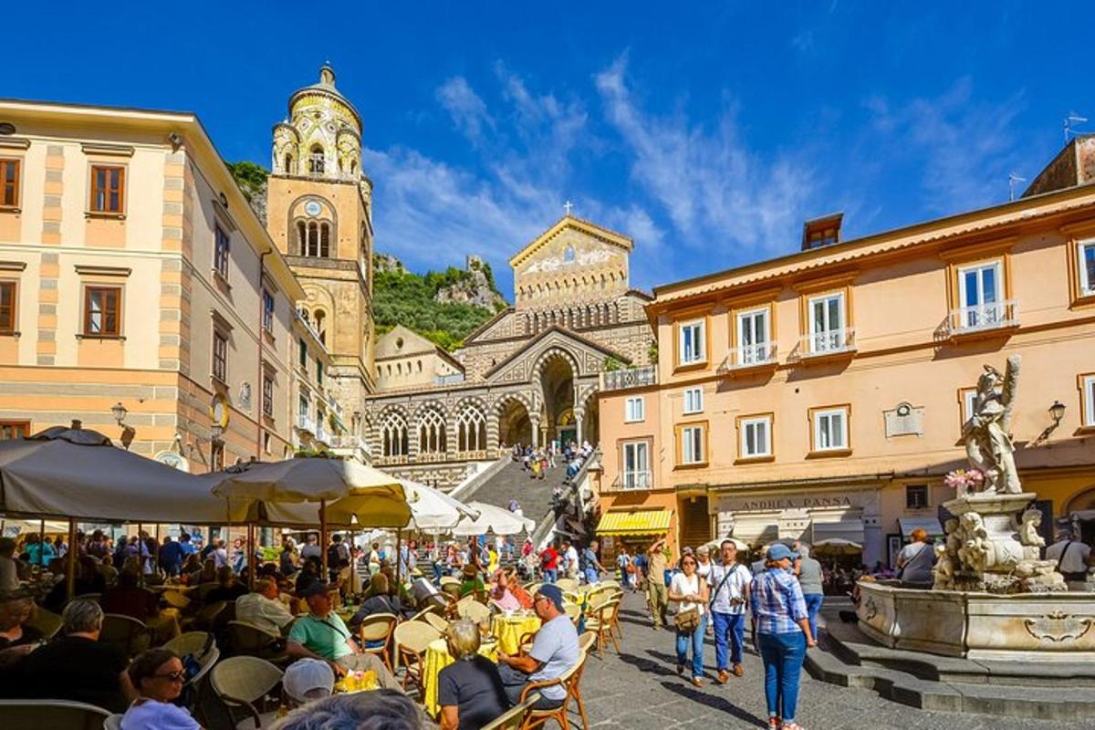 una folla di persone sedute ai tavoli in una strada con una torre dell'orologio