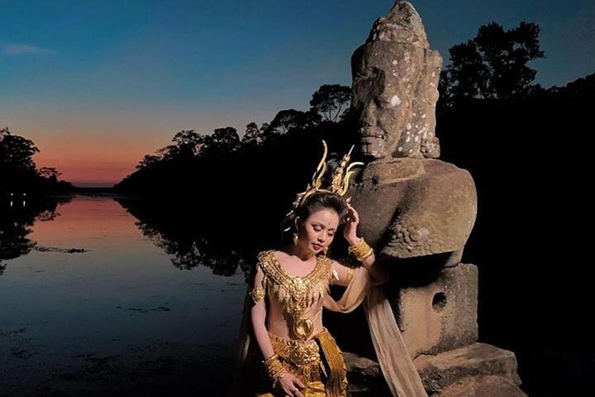 Una mujer con un vestido dorado sentada junto a una estatua.