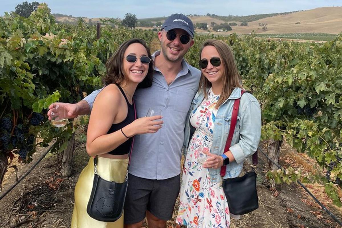 three people posing for a picture in a vineyard