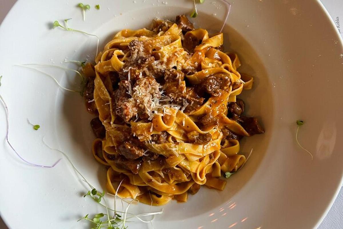 a white plate of pasta with meat and sauce