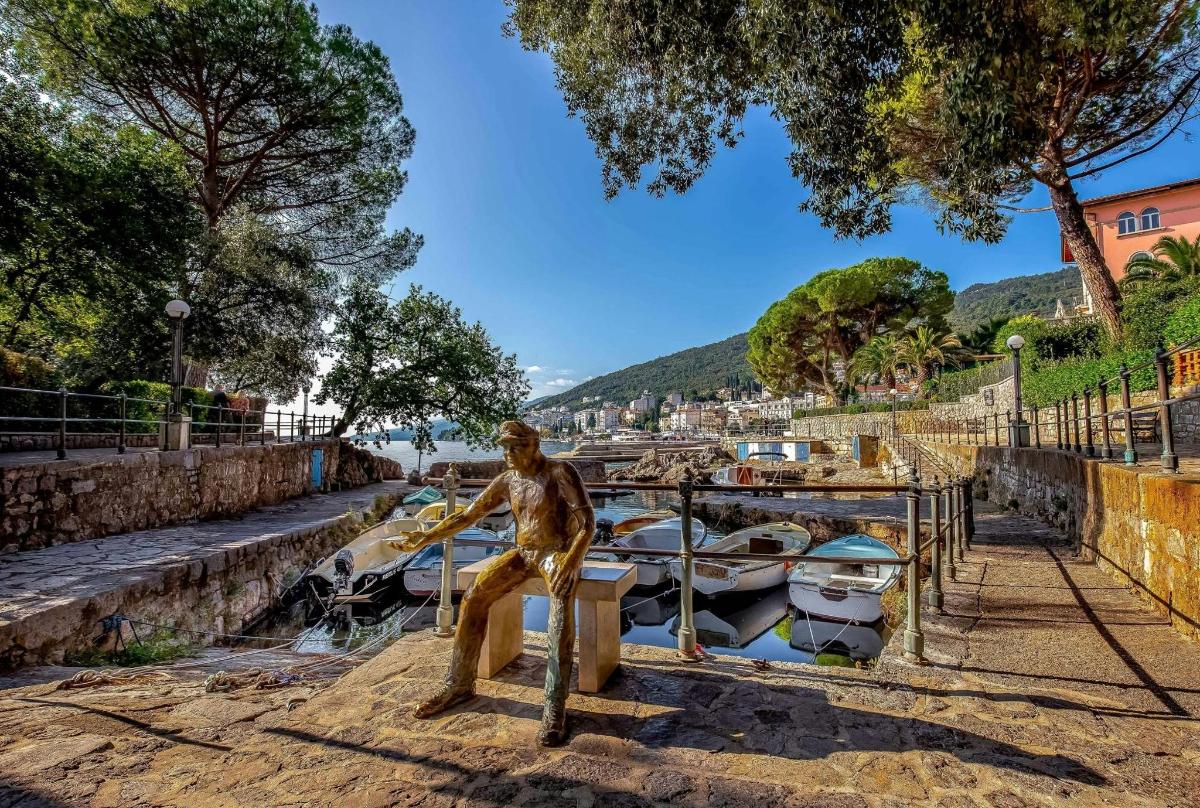 a statue of a man sitting on a bench next to boats