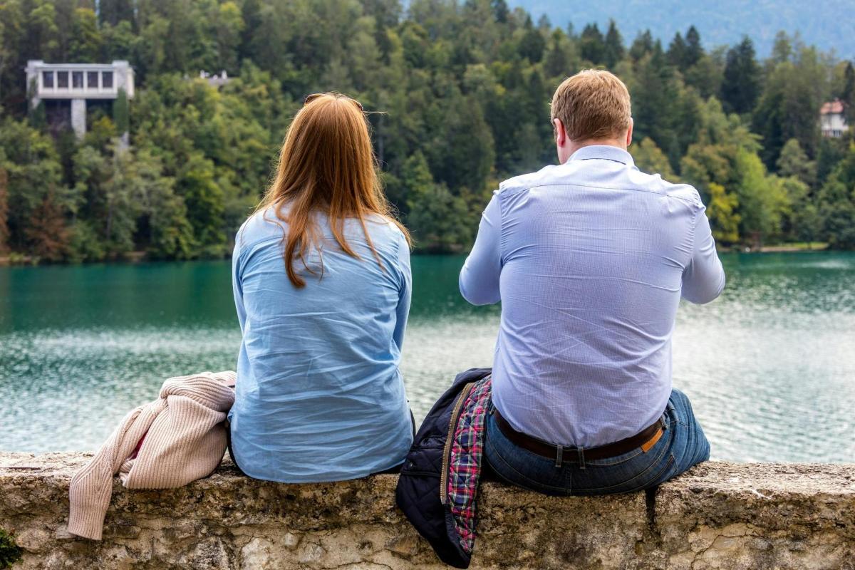 muž a žena sedící na zdi s výhledem na jezero