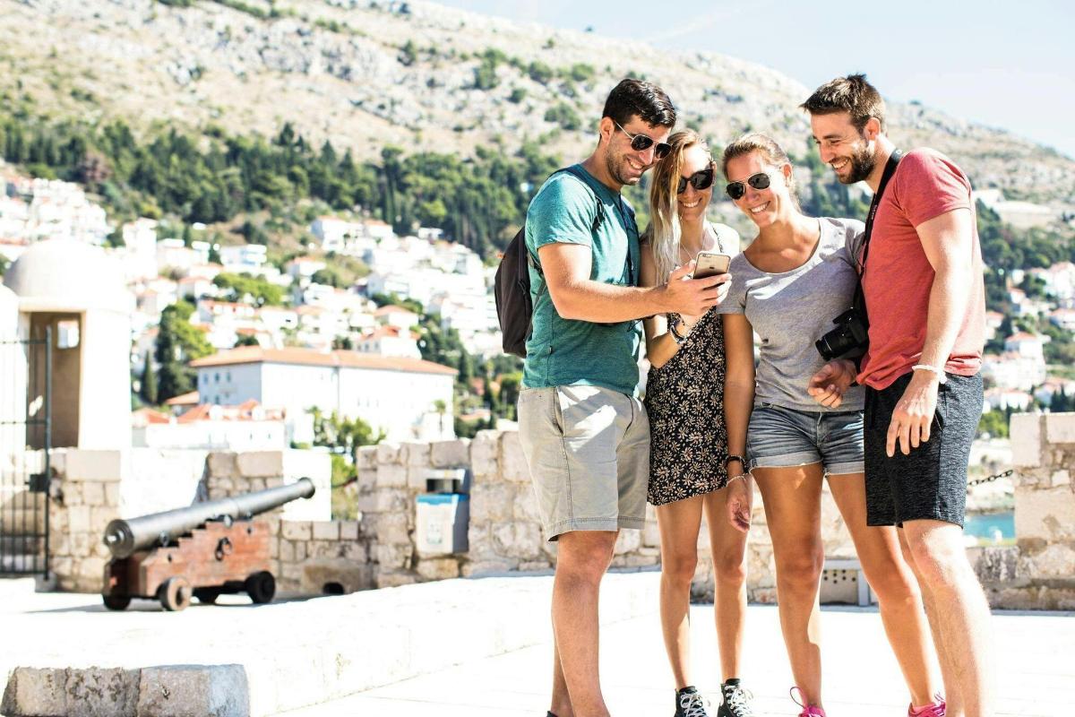trys žmonės stovi vienas šalia kito ir žiūri į mobilųjį telefoną