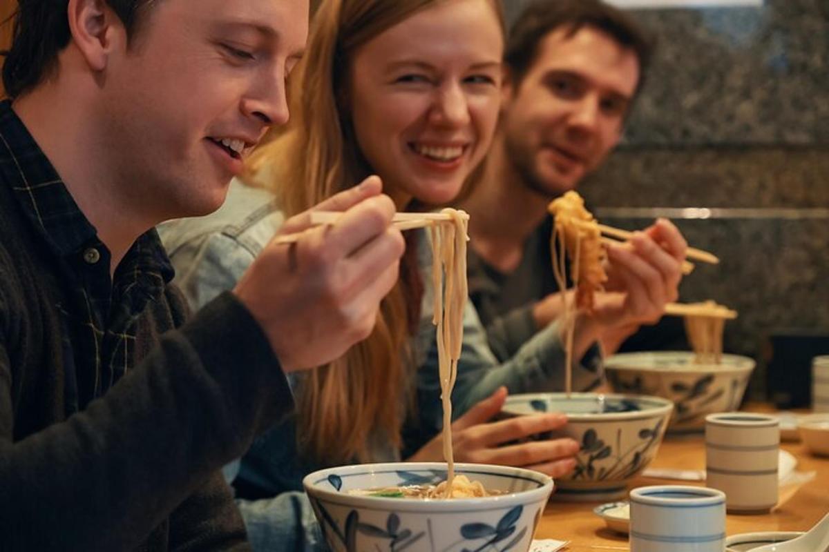 tiga orang duduk di meja makan mie dengan sumpit