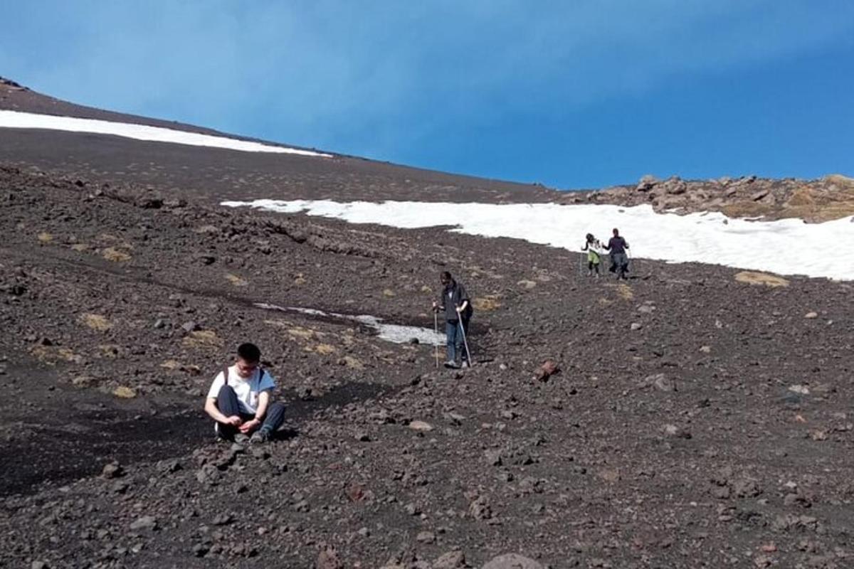 un grup de persones caminant per un turó rocós amb neu