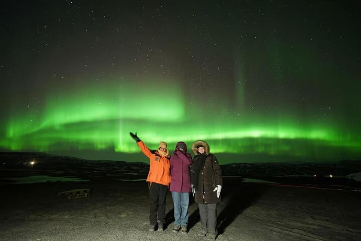 tres persones dempeus sota les aurores boreals verdes