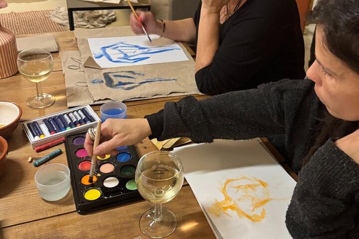 een vrouw die aan een tafel zit en een schilderij maakt met een wijnglas