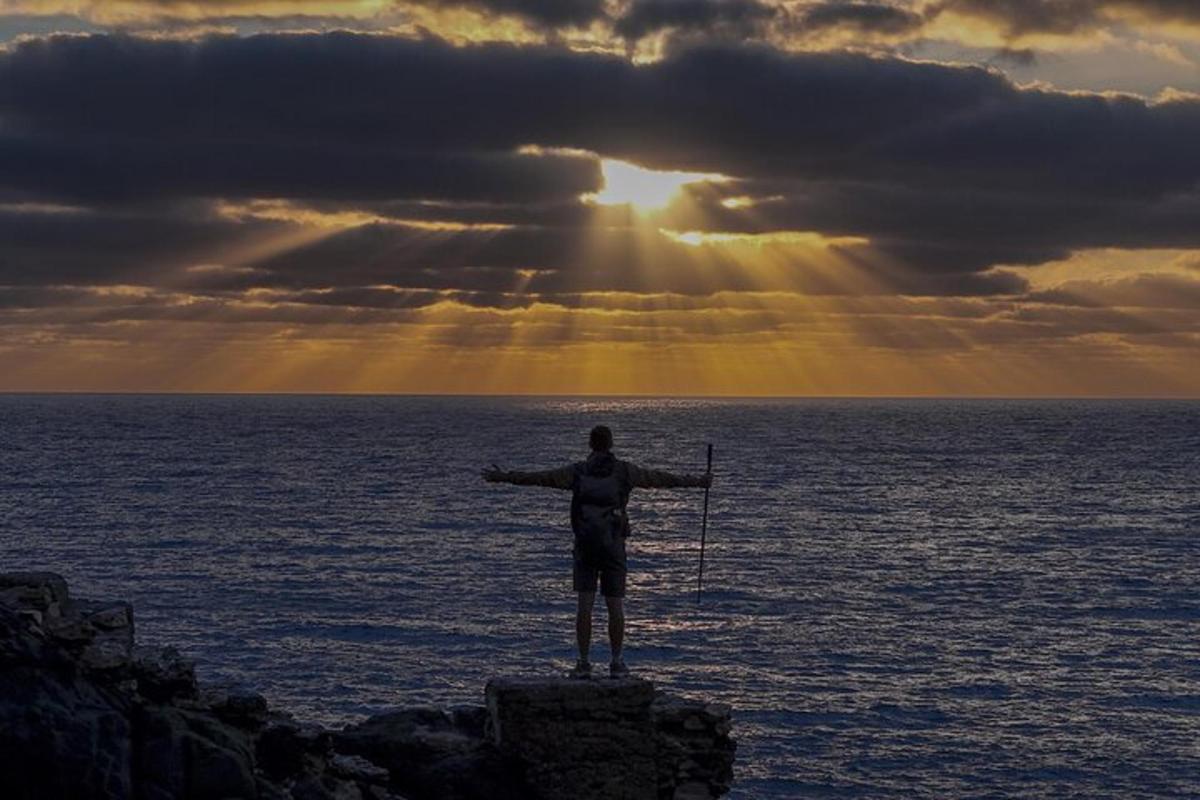 moški, ki stoji na skali v oceanu z iztegnjenimi rokami