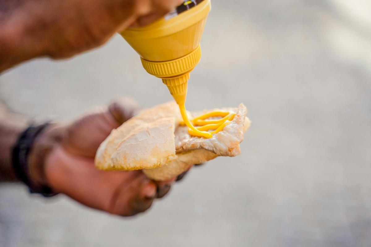 egy személy mustáros hot dogot tart a kezében