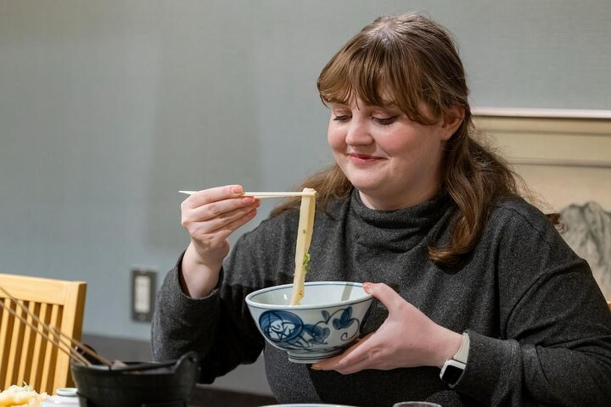 a woman sitting at a table eating a bowl with chopsticks