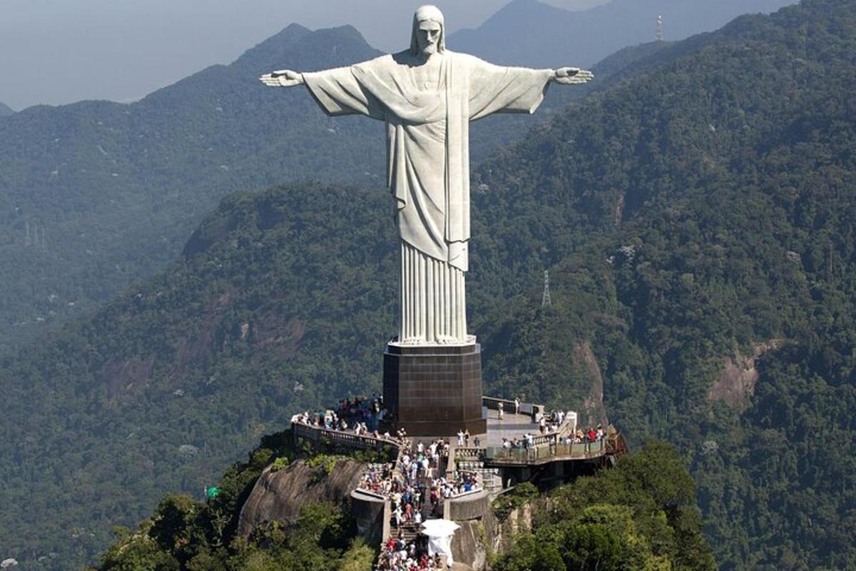 uma multidão de pessoas em pé ao redor da estátua do Cristo Redentor