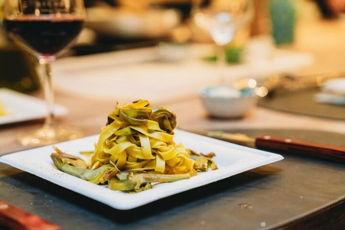 Un plato de pasta en una mesa con una copa de vino.