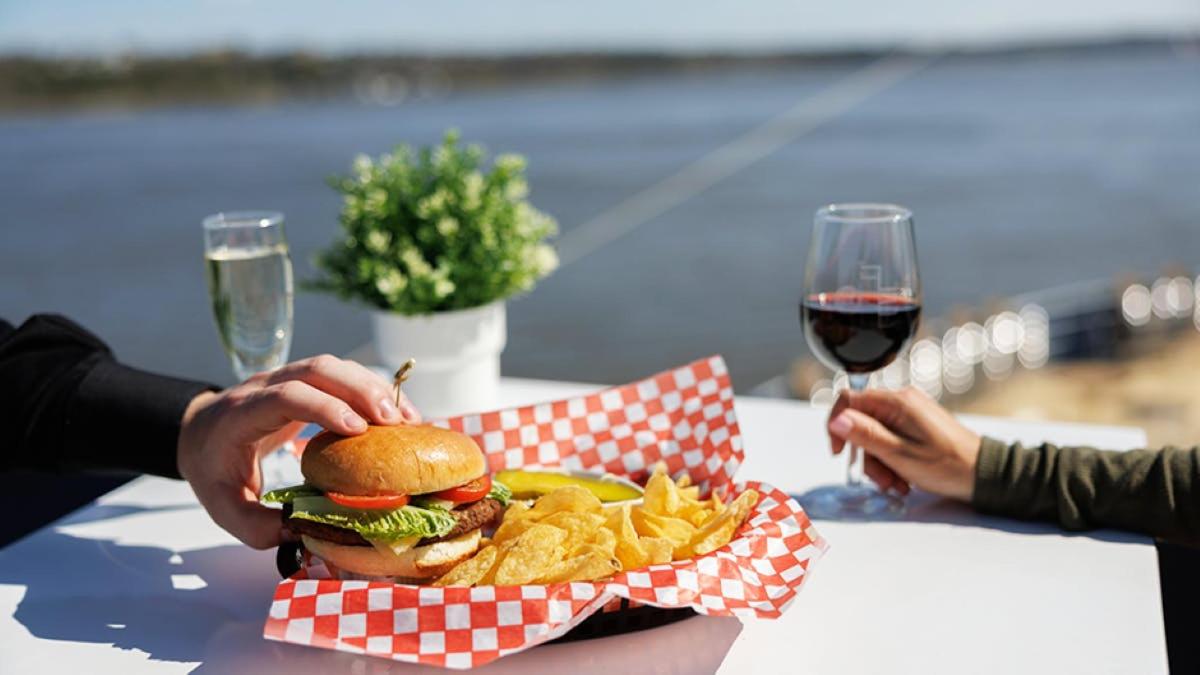 a person holding a hamburger and chips and a glass of wine