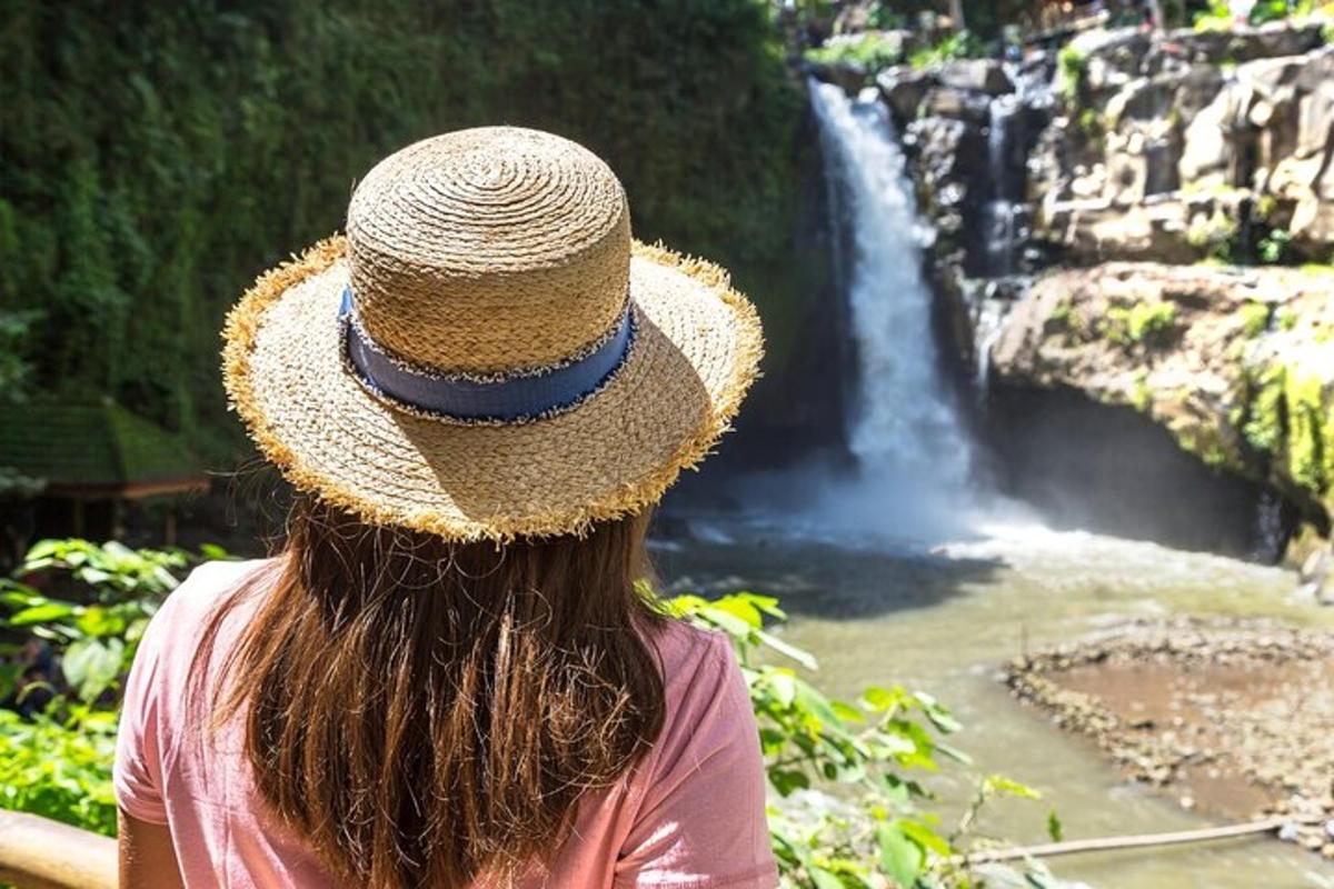 a woman wearing a straw hat looking at a waterfall