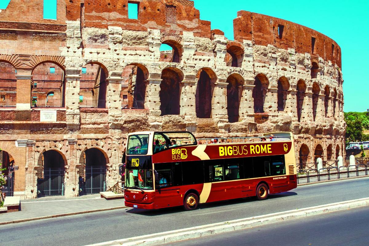 a red double decker bus driving past a building
