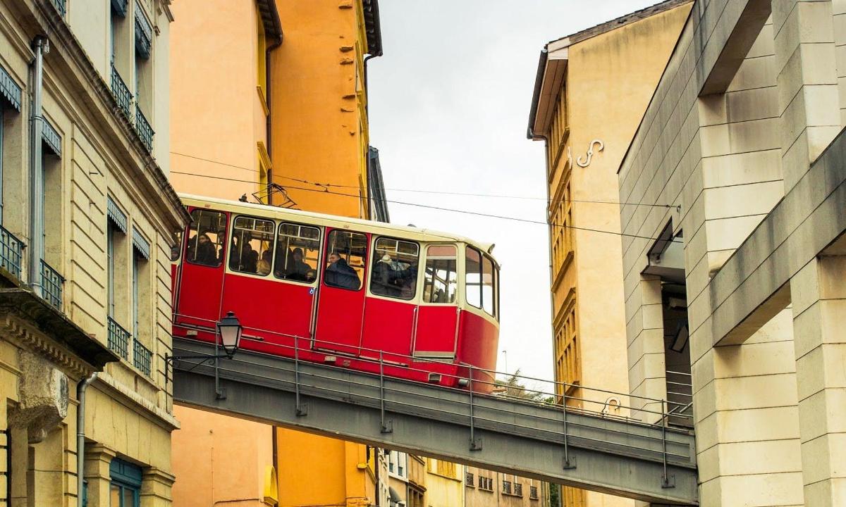 a red tram on a bridge between buildings