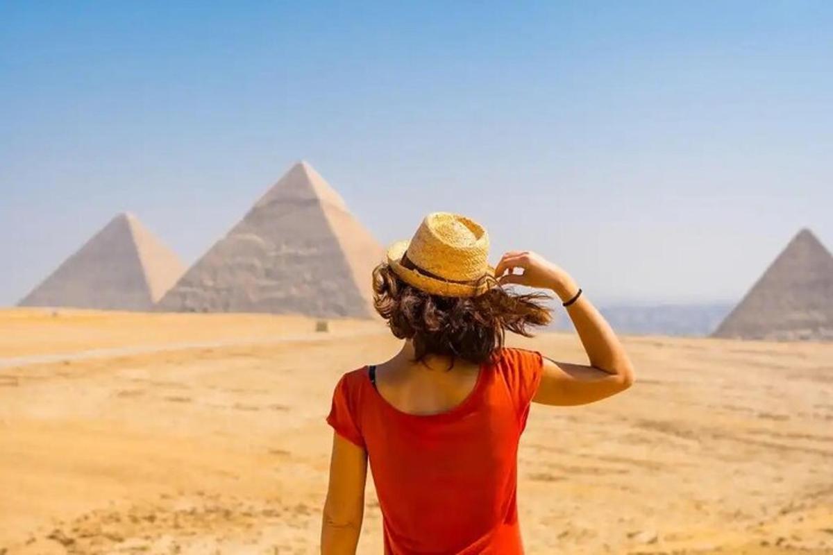 امرأة ترتدي قبعة وتقف أمام الأهرامات