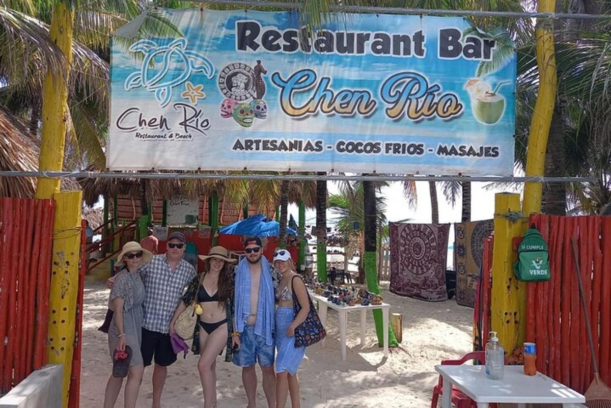 Un grupo de personas de pie bajo un cartel en la playa.