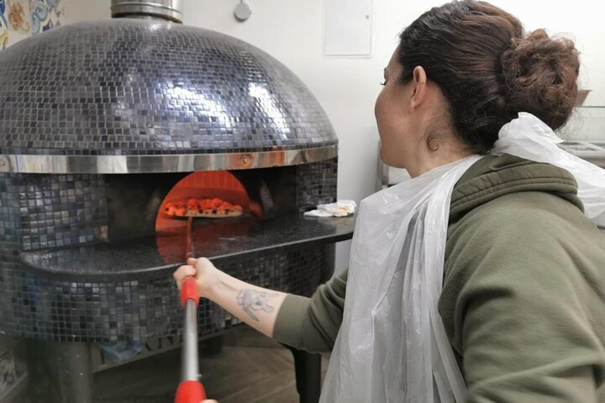 a woman putting a pizza into an oven
