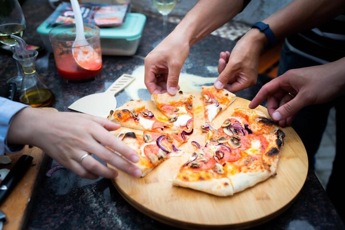 egy csoport ember nyúl egy vágódeszkán lévő pizzáért