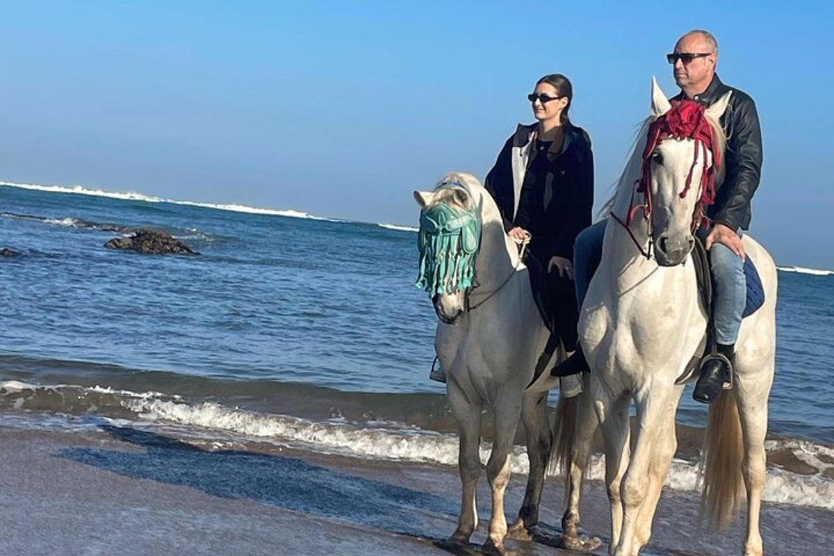 a man and a woman riding horses on the beach