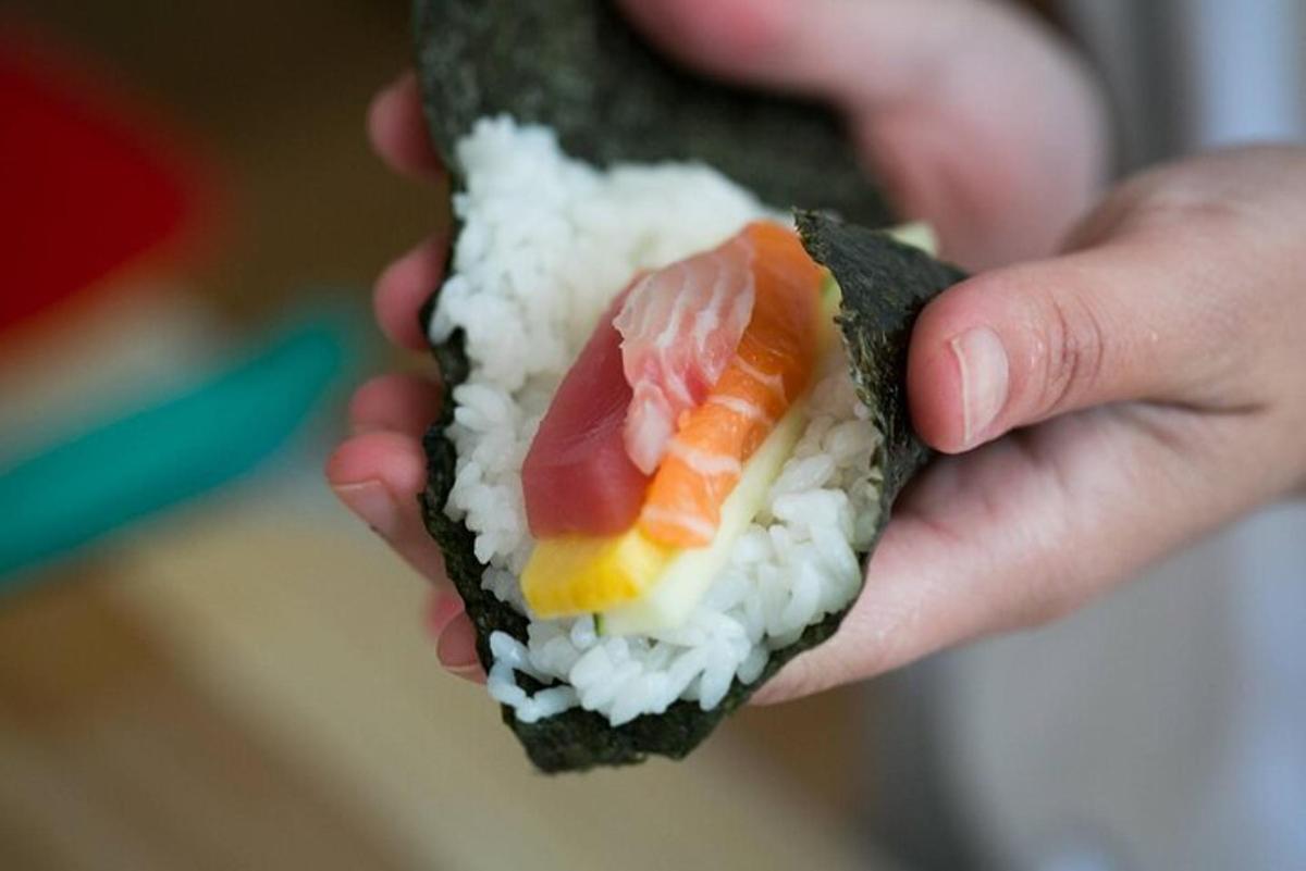 a person holding a piece of sushi with meat and rice