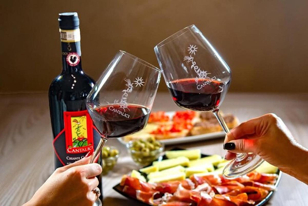 Dos personas sosteniendo copas de vino frente a un plato de comida.