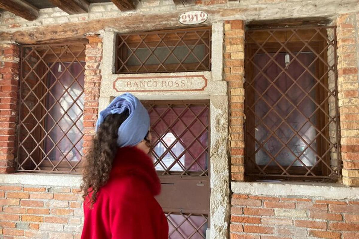ženska, ki gre mimo okna z rešetkami v opečnati stavbi