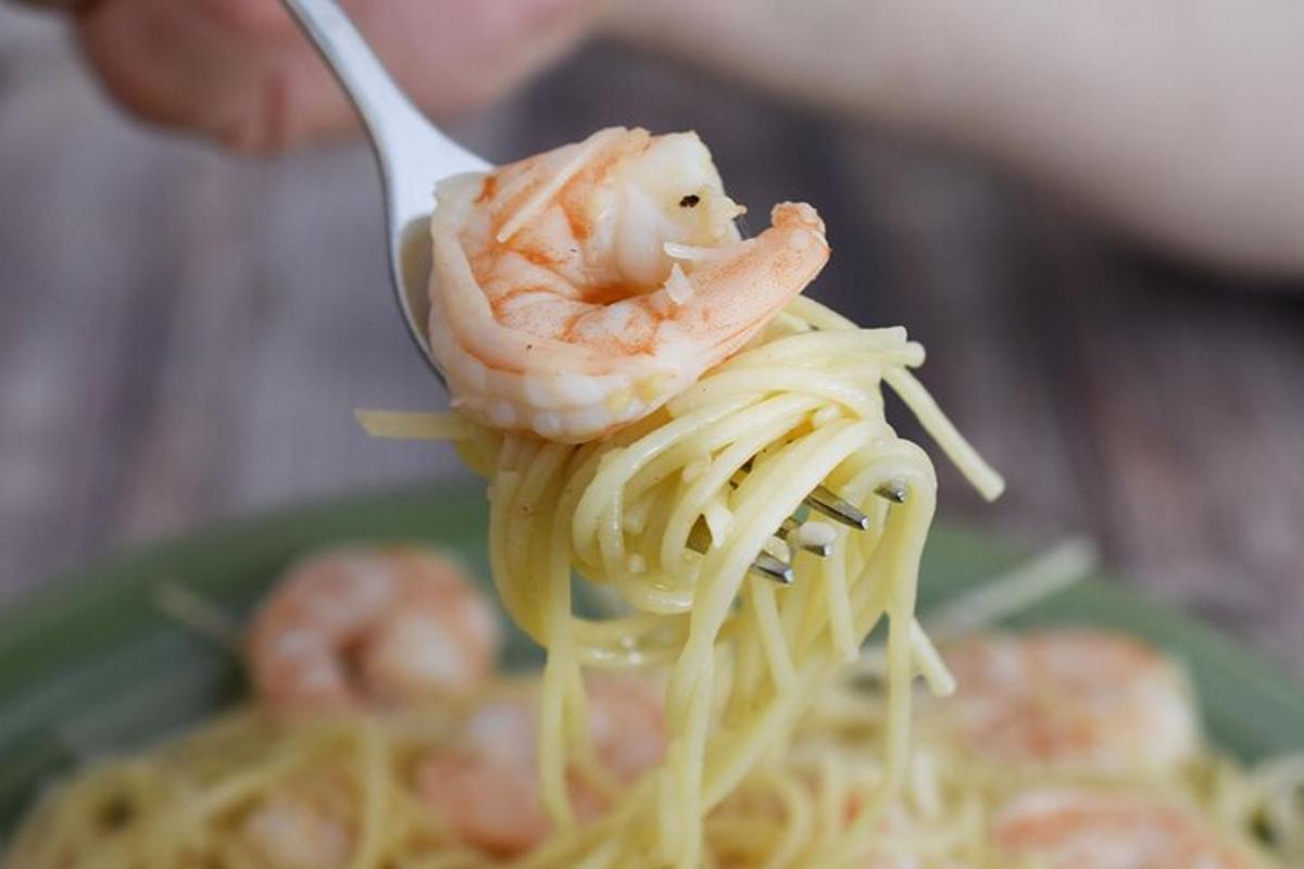 a person holding shrimp on top of pasta on a fork