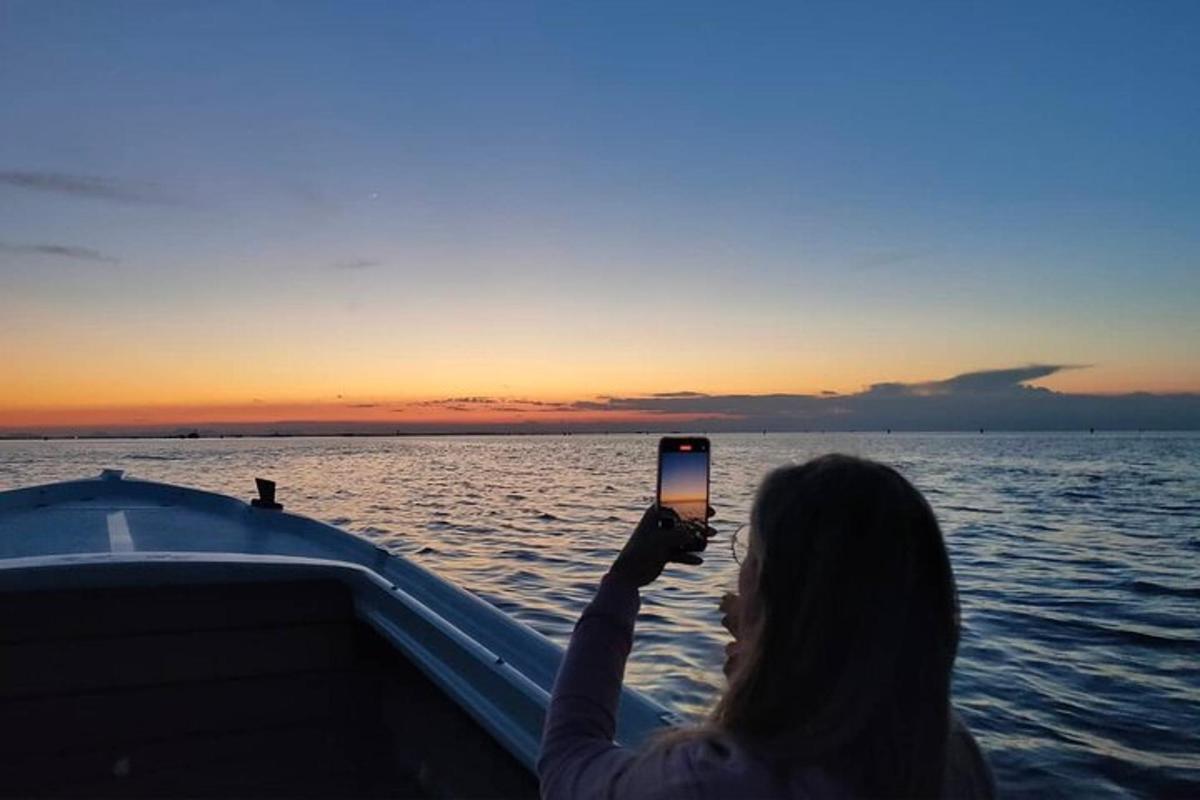 жінка фотографує захід сонця на човні