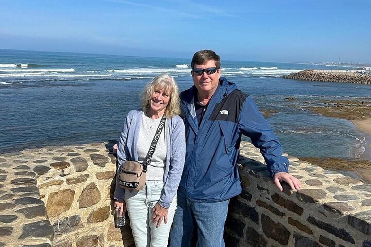 um homem e uma mulher em pé em um muro perto do oceano