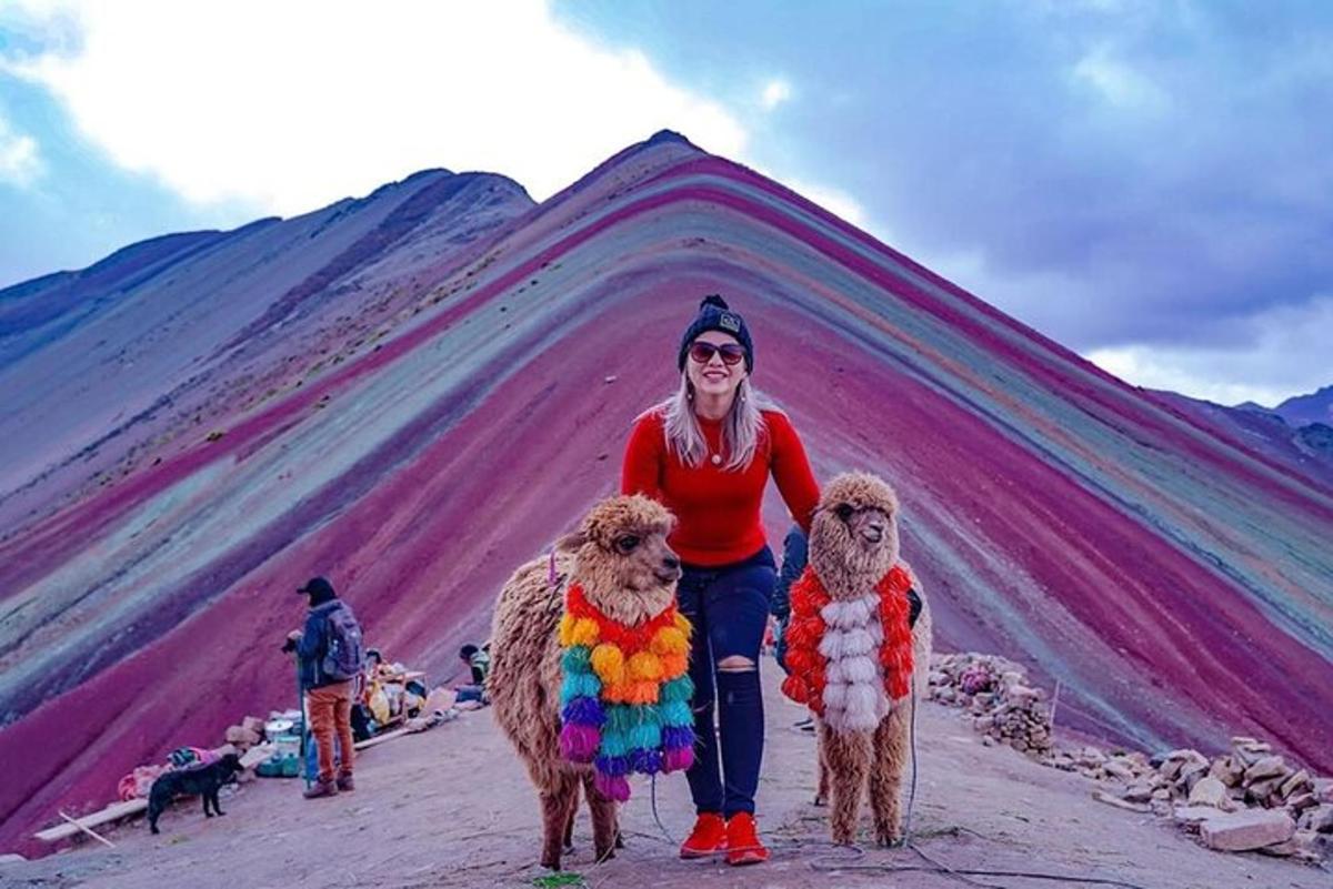 a woman standing next to two sheep in front of a mountain