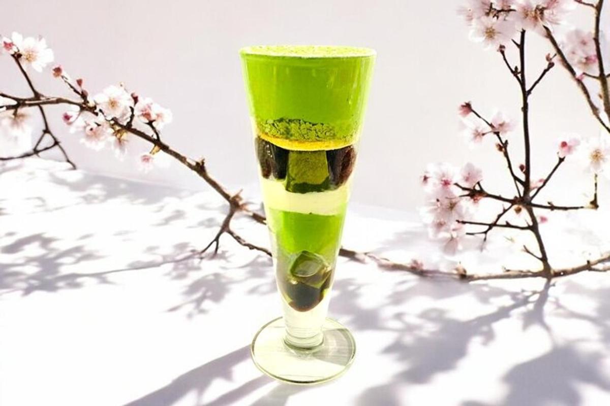 Una bebida verde en un vaso junto a la rama de un árbol.