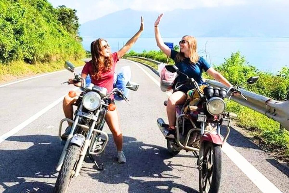 dvě ženy jedoucí na motorkách po silnici s rukama ve vzduchu