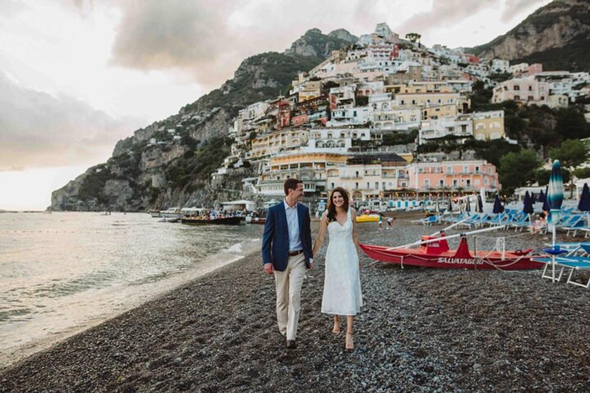 una sposa e uno sposo che camminano sulla spiaggia con positano
