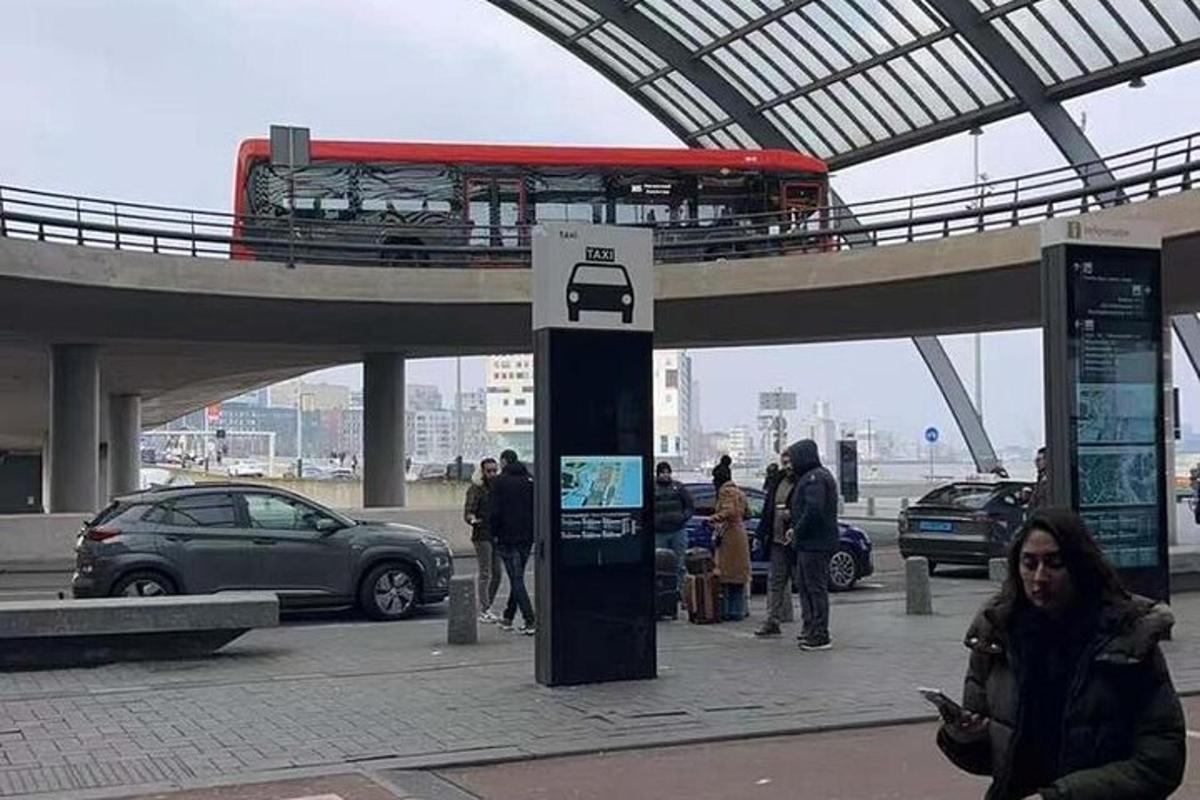 un autobus rosso che passa sotto un ponte con persone che camminano