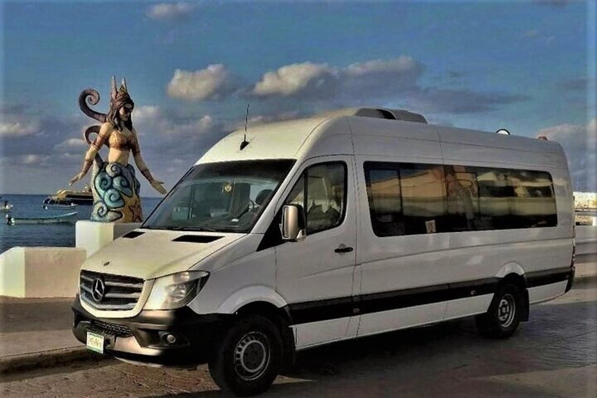 Una camioneta blanca con una mujer parada junto al océano.