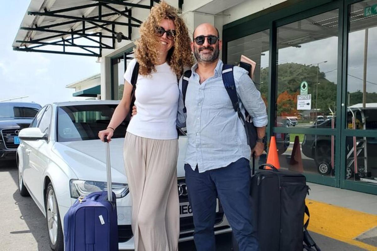 moški in ženska stojita poleg avtomobila s prtljago