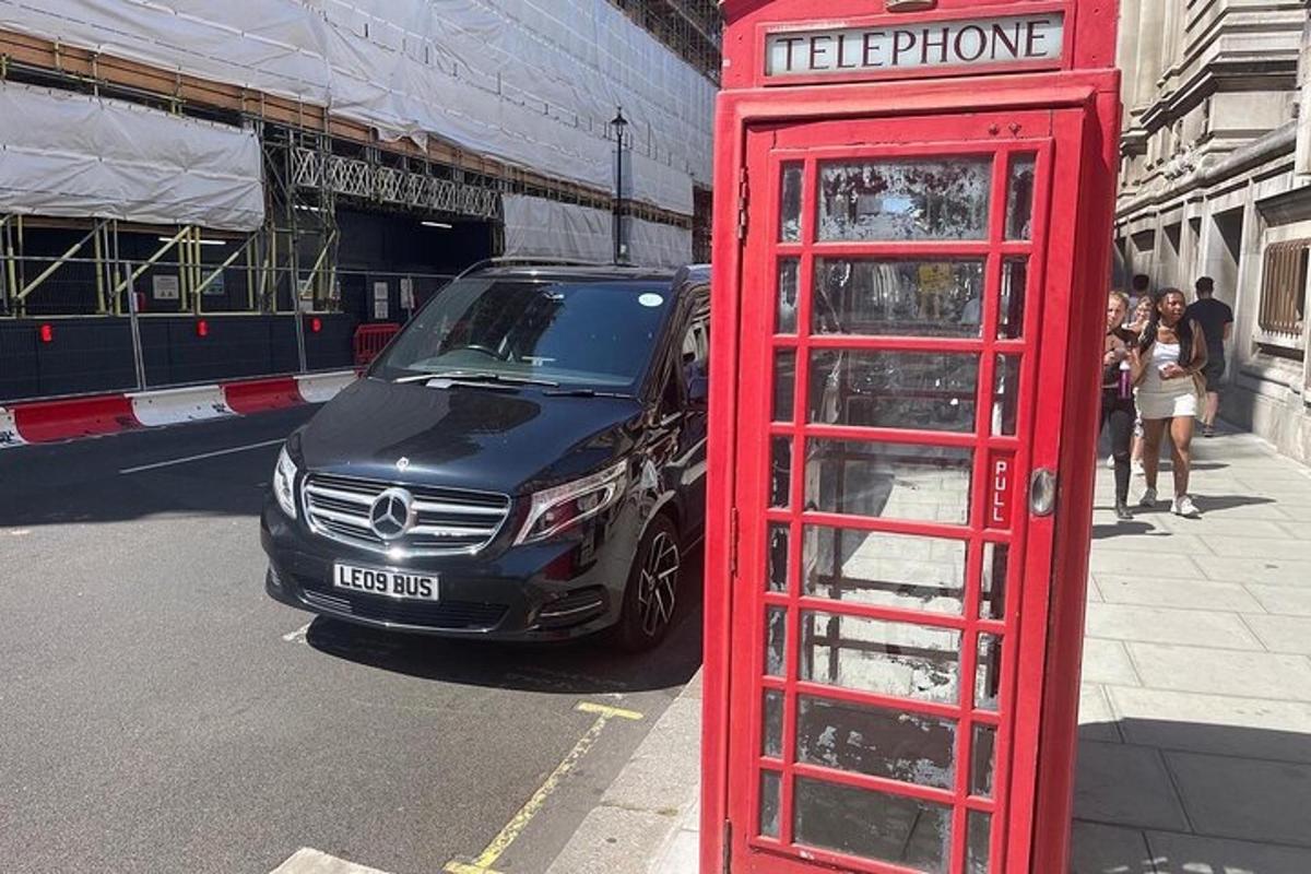 uma cabine telefônica vermelha e um carro estacionado na rua