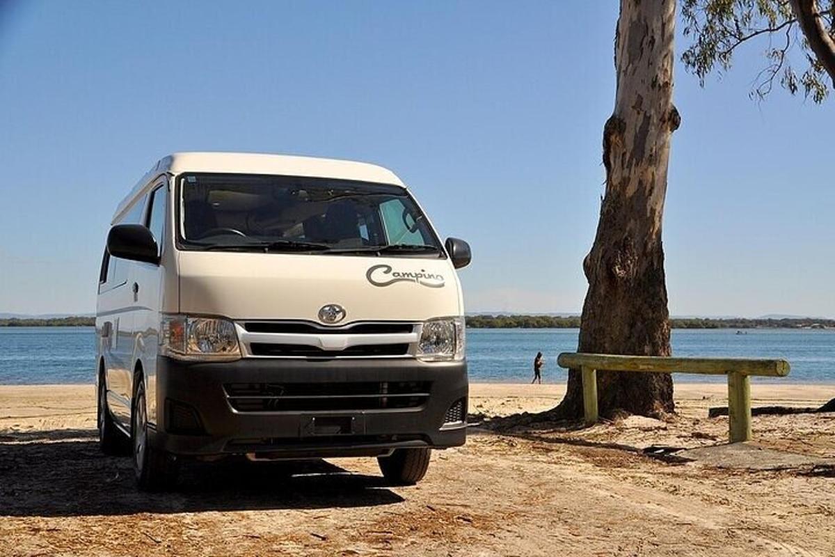 un furgone bianco parcheggiato accanto a un albero sulla spiaggia