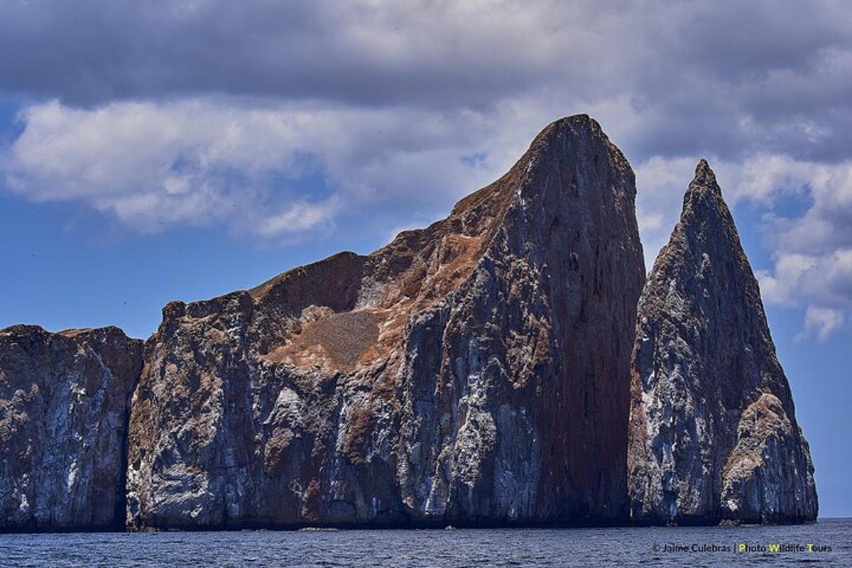 a large rocky mountain in the water with a cloudy sky