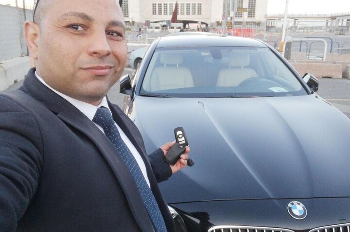 muž v obleku držící mobilní telefon vedle auta