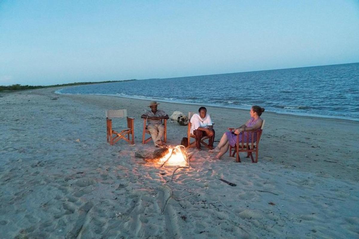 three people sitting around a fire on the beach