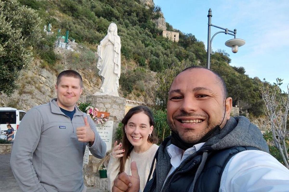 três pessoas fazendo sinal de positivo em frente a uma estátua