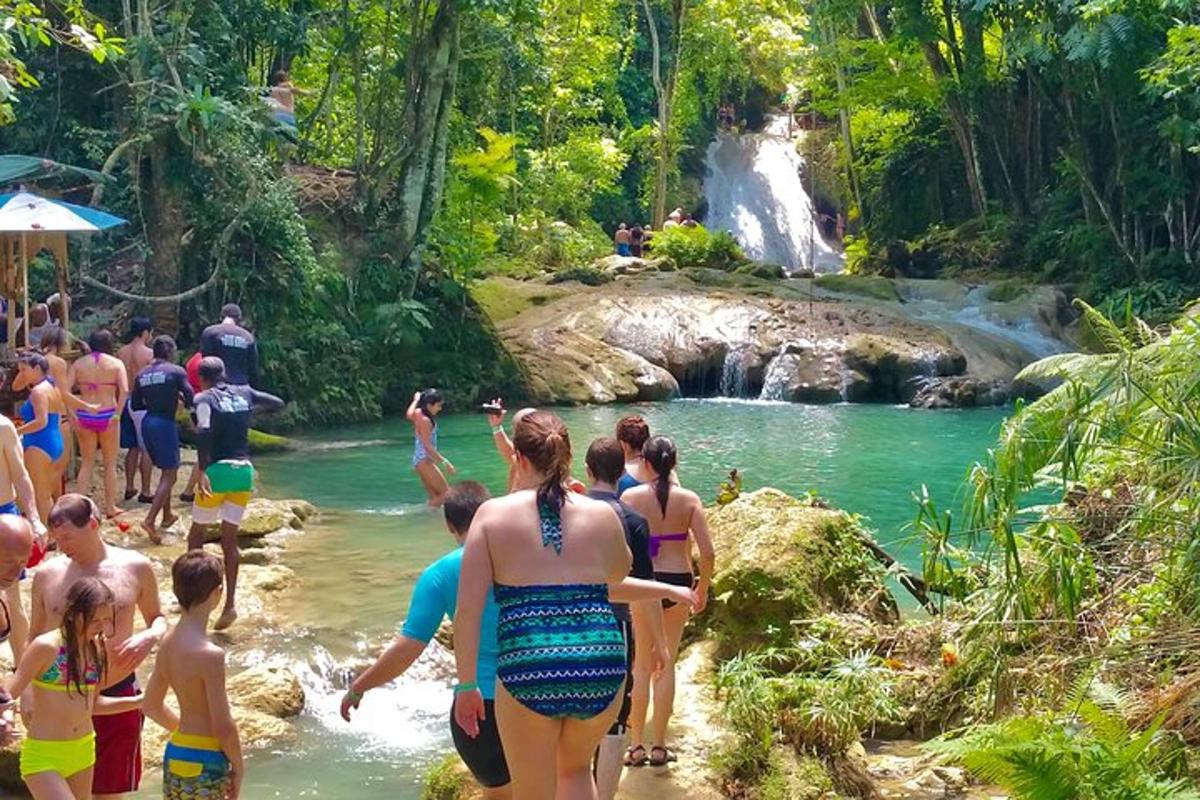 um grupo de pessoas em pé na água em frente a uma cachoeira