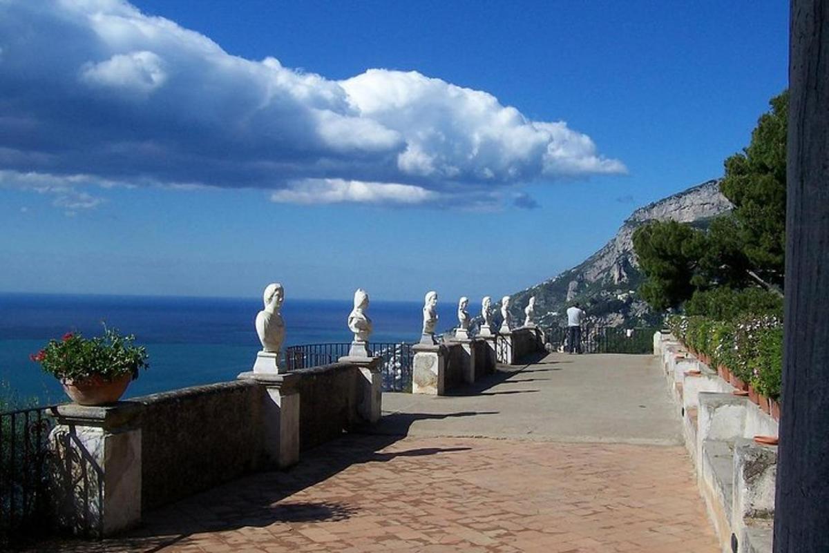 a walkway with statues and the ocean in the background