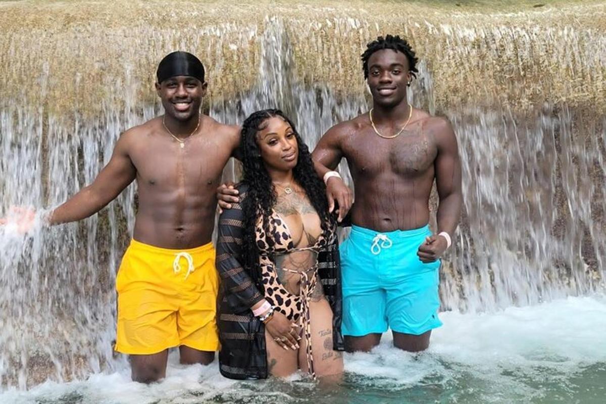Tres personas paradas en el agua frente a una cascada.