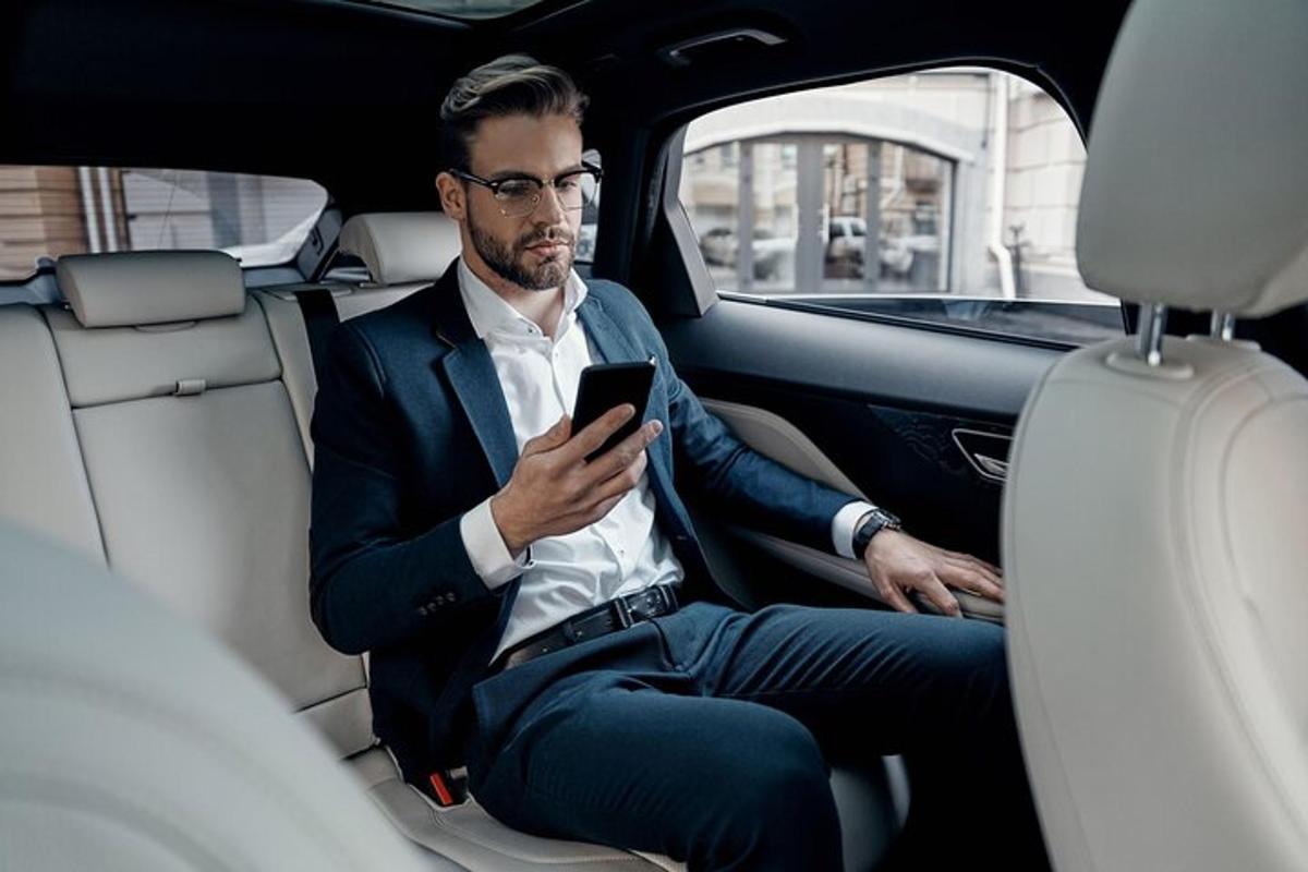 Un hombre sentado en el asiento trasero de un coche mirando su teléfono móvil.